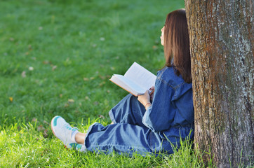 Naklejka na ściany i meble Young pretty student woman is sitting near the tree with a book