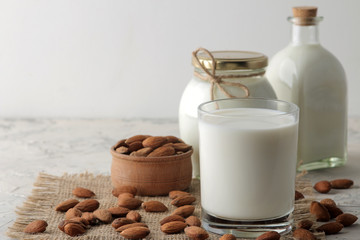 Fresh almond milk in a glass and almond nuts on a light background