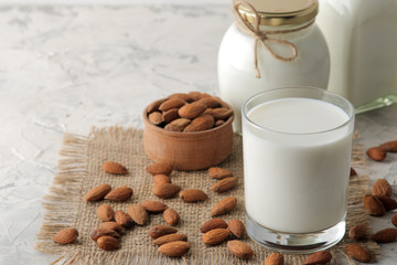 Fresh almond milk in a glass and almond nuts on a light background