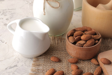 Fresh almond milk in a milk jug and almond nuts on a light background