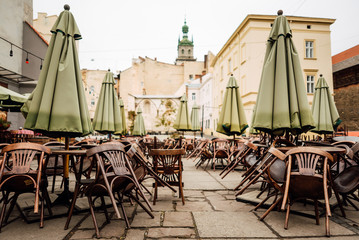 Cafe tables and chairs outside with large green umbrellas. Old beautiful city