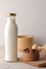 Fresh almond milk in a glass bottle and almond nuts on a light background