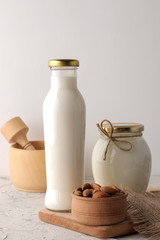 Fresh almond milk in a glass bottle and almond nuts on a light background
