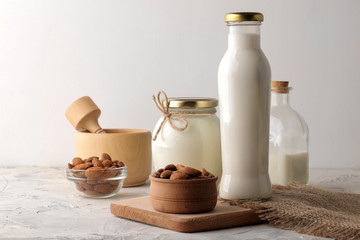 Fresh almond milk in a glass bottle and almond nuts on a light background