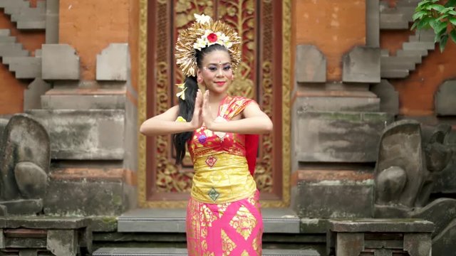 Slow motion of beautiful balinese dancer with traditional dress, showing welcoming gesture in a temple