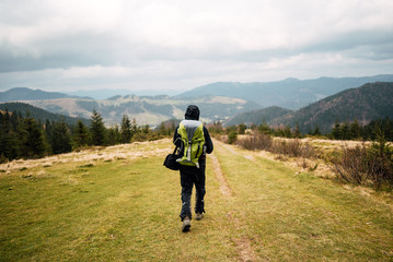 Man with a backpack walking along the road. There are mountains on the horizon. The sky is blue and cloudy.