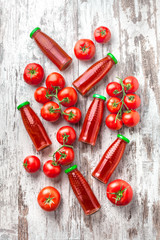 Tomato cooked fresh juice in bottles with cherry tomatoes overhead arrangement on white wooden table studio shot