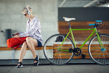 Fototapeta na wymiar Image of young woman in headphones sitting on bench next to green bicycle