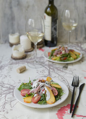 Salad with persimmon, smoked chicken, cherry tomatoes, Camembert cheese and blue cheese sauce. Festive dish on a white wooden table with a glass of white wine. Christmas dinner. Selective focus.