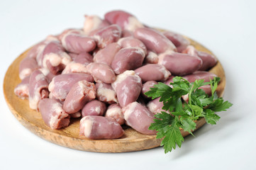 Raw chicken hearts on a round wooden tray. The product is decorated with parsley. White background. Close-up. 
