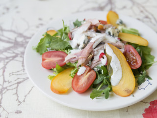 Salad with persimmon, smoked chicken, cherry tomatoes, Camembert cheese and blue cheese sauce. Festive dish . Christmas dinner. Selective focus, closeup, copy space