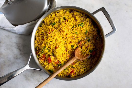 Overhead view of turmeric rice with tomatoes in saucepan