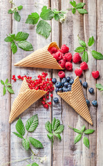 Berries fresh colorful strawberries blackberries red currant raspberries overhead mixed arrangement in ice cream cones on old rustic white wooden table with green leaves studio shot
