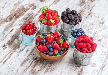 Berries fresh colorful arrangement in tin cans and wooden bowl on old white rustic wooden table front view studio shot