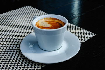 Close up beautiful white coffee cup with foam of morning, breakfast espresso with latte art on the black vintage wooden table Dark black and white space background Trendy toning Hot Latte Art coffee