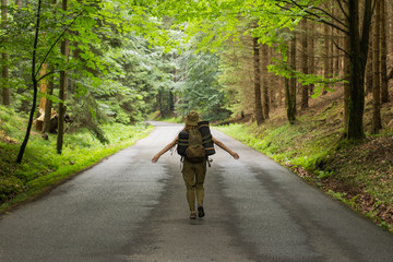 young  woman hiker walking on narrow road through summer green forest