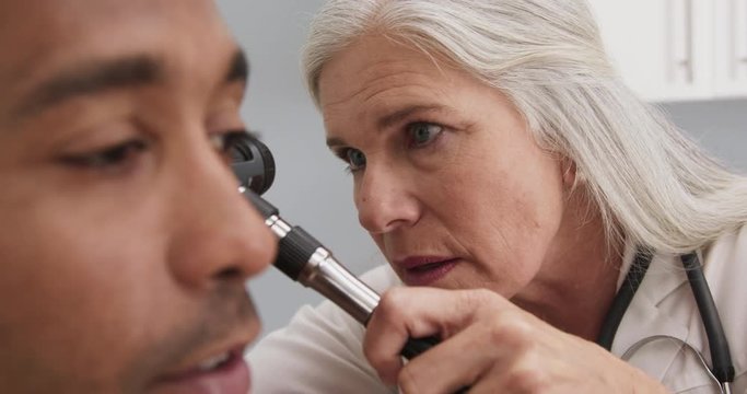 Tight shot of professional senior doctor examining ear of young male patient. Healthy african-american patient meeting with doctor for routine check up