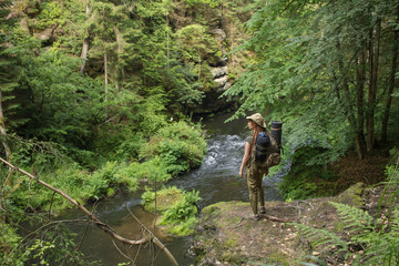 Fototapeta premium Young woman hiker posing near the river in bohemian switzerland national park, female traveler in mountains of czech republic