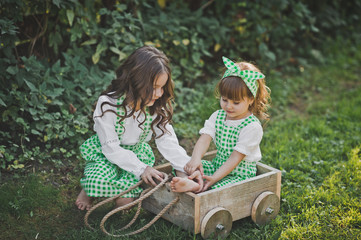 Two sisters play outside with a cart 1877.