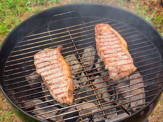 Two juicy beef steaks are grilled on a round grill