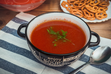 Fresh tomato soup with greens in a bowl on striped tablecloth