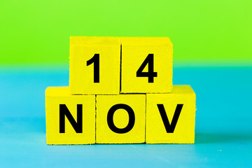 NOV 14, yellow cube calendar on blue wooden surface with copy space