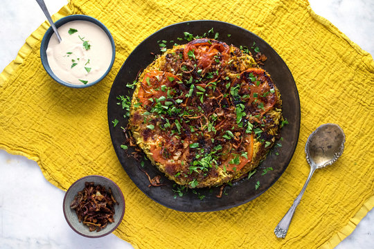 Overhead view of spiced maqluba with tomatoes and tahini sauce