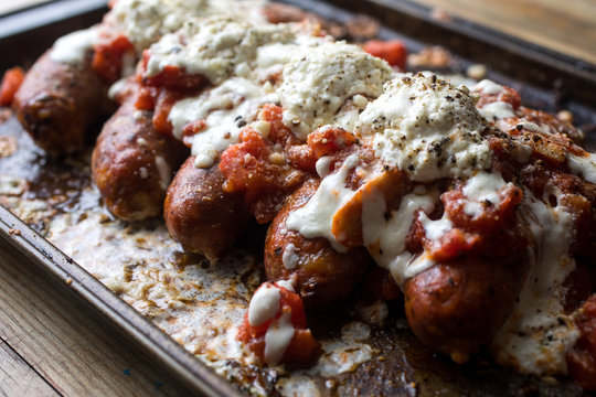 Close up of sausage parmesan with garlicky broccoli on baking tray