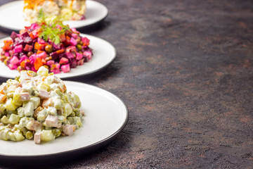 Russian food on dark background. Assortment salad of Russian cuisine - Olivier salad, vinaigrette - beet salad, herring salad. Top view. Copy space.