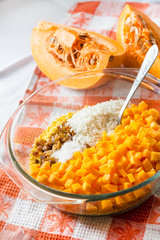 Raw washed millet, rice, raisins and pumpkin in a glass pan in the process of preparing milk pumpkin porridge