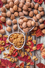 Walnuts overhead arrangement in white heart shaped ceramic jars with red leaves on white rustic wooden table in studio