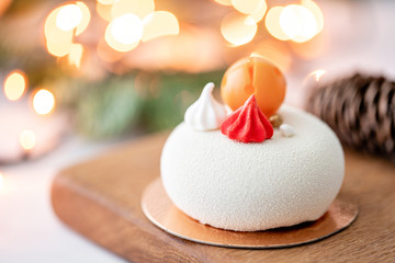 Mini mousse pastry dessert covered with white velour on garland lamps bokeh background. Modern european cake. French cuisine. Christmas theme