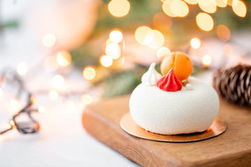 Mini mousse pastry dessert covered with white velour on garland lamps bokeh background. Modern...