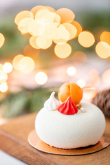 Mini mousse pastry dessert covered with white velour on garland lamps bokeh background. Modern european cake. French cuisine. Christmas theme
