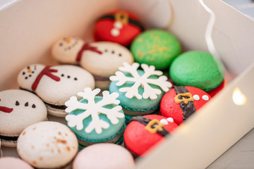 Variety of sweet macaroons in white box. The branches of spruce on bokeh background. Modern european French cuisine. Christmas theme, Merry Christmas card. New year mood. lights of garland bulbs