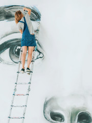 Graffiti Artist Drawing face of beautiful woman with paint on Street Wall. Female working with brush. Urban Outdoors Art Concept