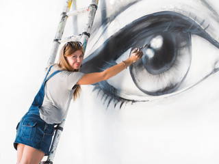 Graffiti Artist Drawing face of beautiful woman with paint on Street Wall. Female working with...