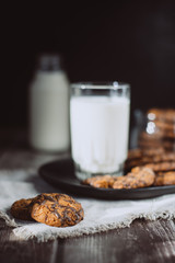 Glass with fresh milk and homemade chocolate chips cookies over a wooden table. 