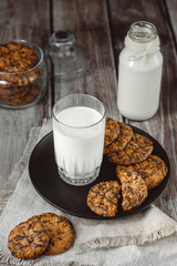 Glass with fresh milk and homemade chocolate chips cookies over a wooden table. 