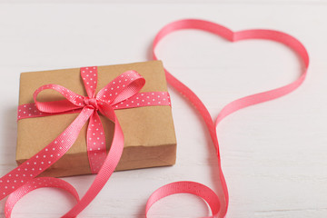 A gift of craft paper and a pink ribbon on a white wooden table. Place for text, copy space, Valentine's day postcard.