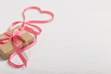 A gift of craft paper and a pink ribbon on a white wooden table. Place for text, copy space,...