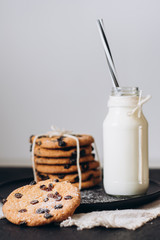 Glass with fresh milk and homemade chocolate chips cookies over a dark table. 