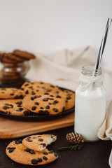Glass with fresh milk and homemade chocolate chips cookies over a dark table. 