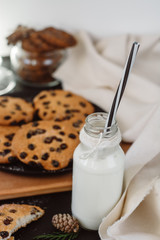 Glass with fresh milk and homemade chocolate chips cookies over a dark table. 