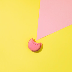 Bitten cake macaron or macaroon on yellow and pink background from above, colorful almond cookies, minimalism, sharp shadow