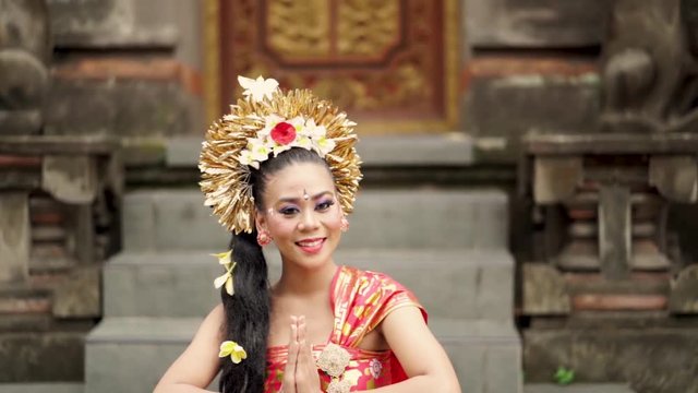Pretty balinese woman showing welcome gesture while wearing traditional dress in a hinduism temple. Shot outdoors
