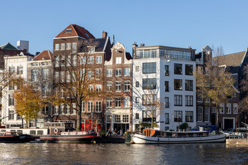 Fototapeta na wymiar Typical Amsterdam canal houses with residential boats in front and a tourist ship passing by on a sunny day in late afternoon