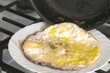 Put the scrambled eggs with sausage from a frying pan on gas stove to the white plate.