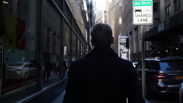 Young confident businessman walking through New York city streets in daytime at Wall Street slowmo.