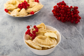 A portion of boiled dumplings with a piece of butter and red viburnum berries, wooden background.